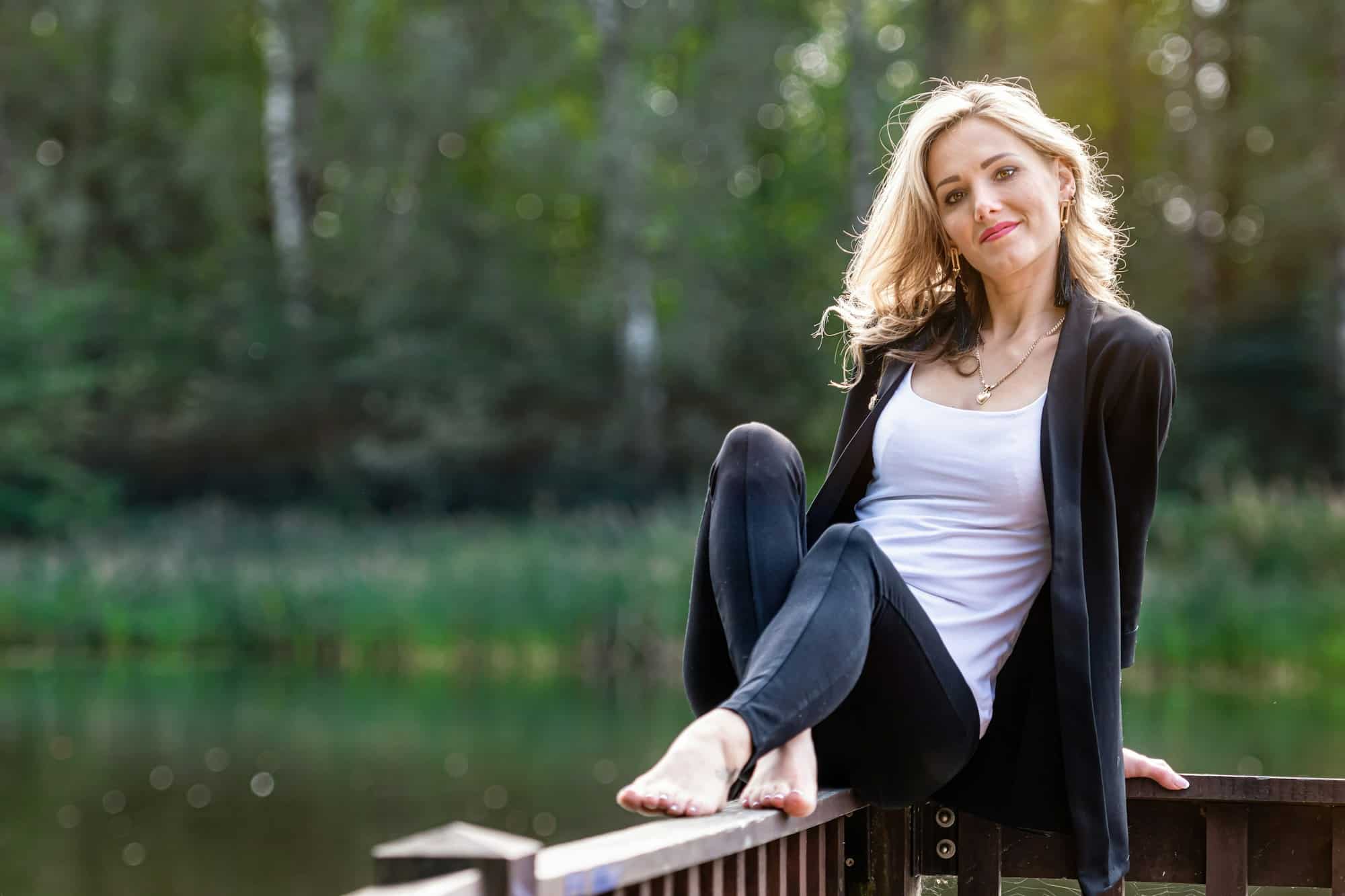 young positive, smiling female sits on the wooden railings of the pier